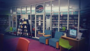 Chairs and computers line a glass wall. The sign - Frank Weaner Teen Room hangs over the door and book are seen within the teen space