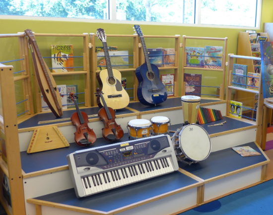 Guitars, drums, violins, a dulcumer, and bells on display in the program area of the kids room.