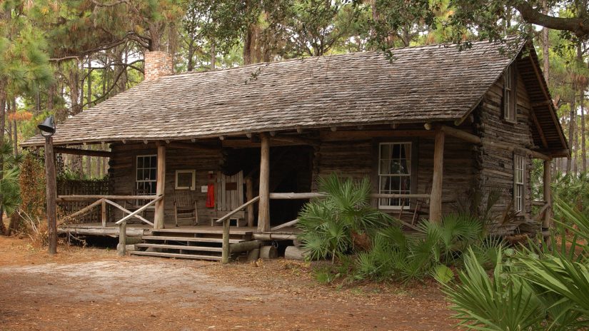 log cabin at Heritage Village with a large fron board nestled in the woods.
